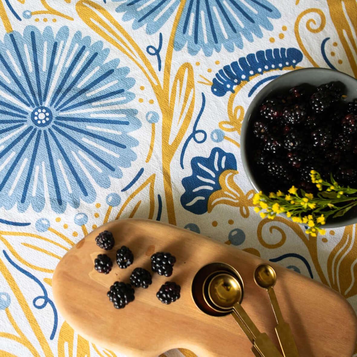 Blackberries on a wooden board with gold spoons against a floral patterned background