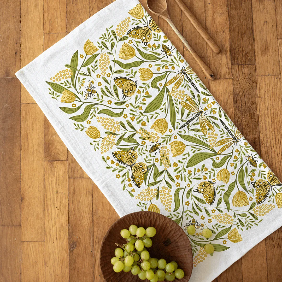 Floral and butterfly patterned tablecloth on a wooden surface with a bowl of grapes.