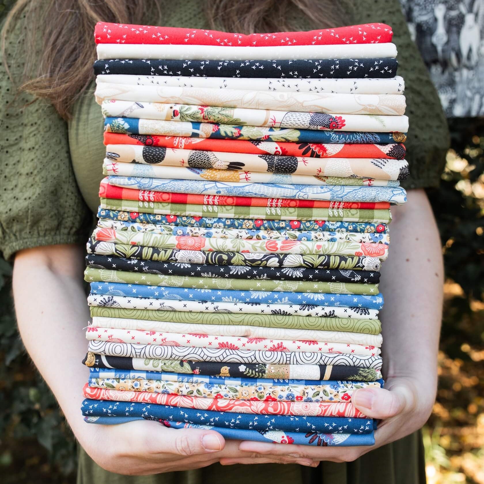 Person holding a stack of colorful fabric bundles outdoors