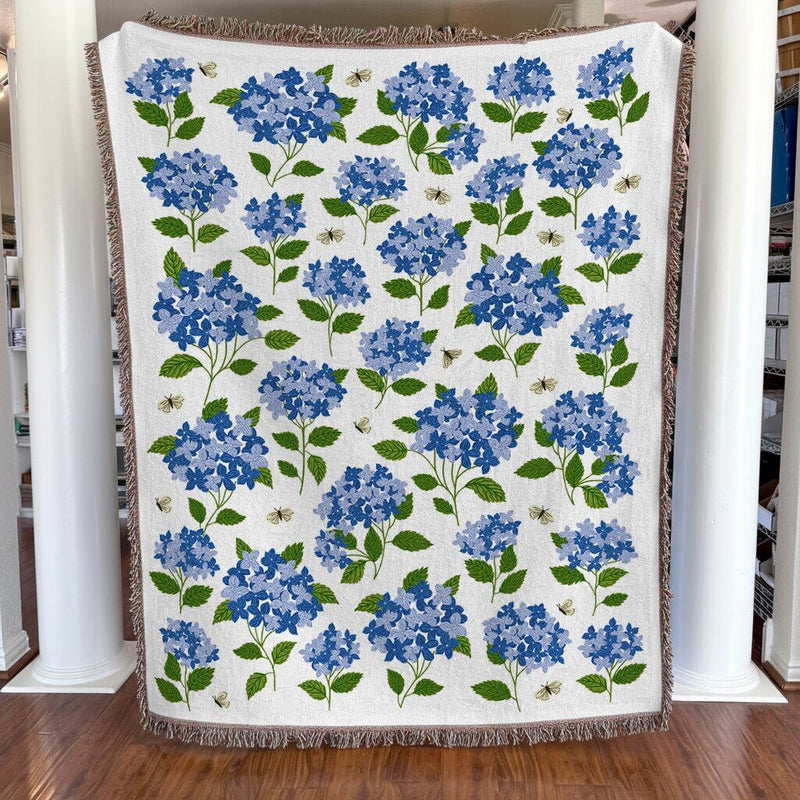 Floral-patterned blanket with blue flowers and green leaves on a wooden floor.
