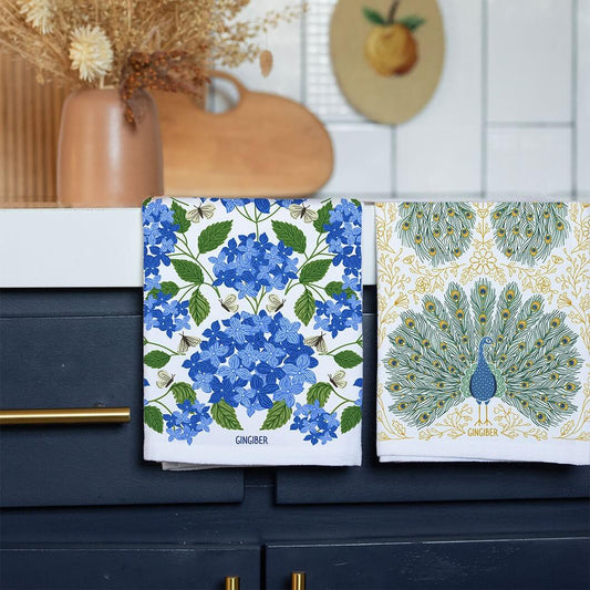 Two decorative towels with floral and peacock designs on a kitchen counter.