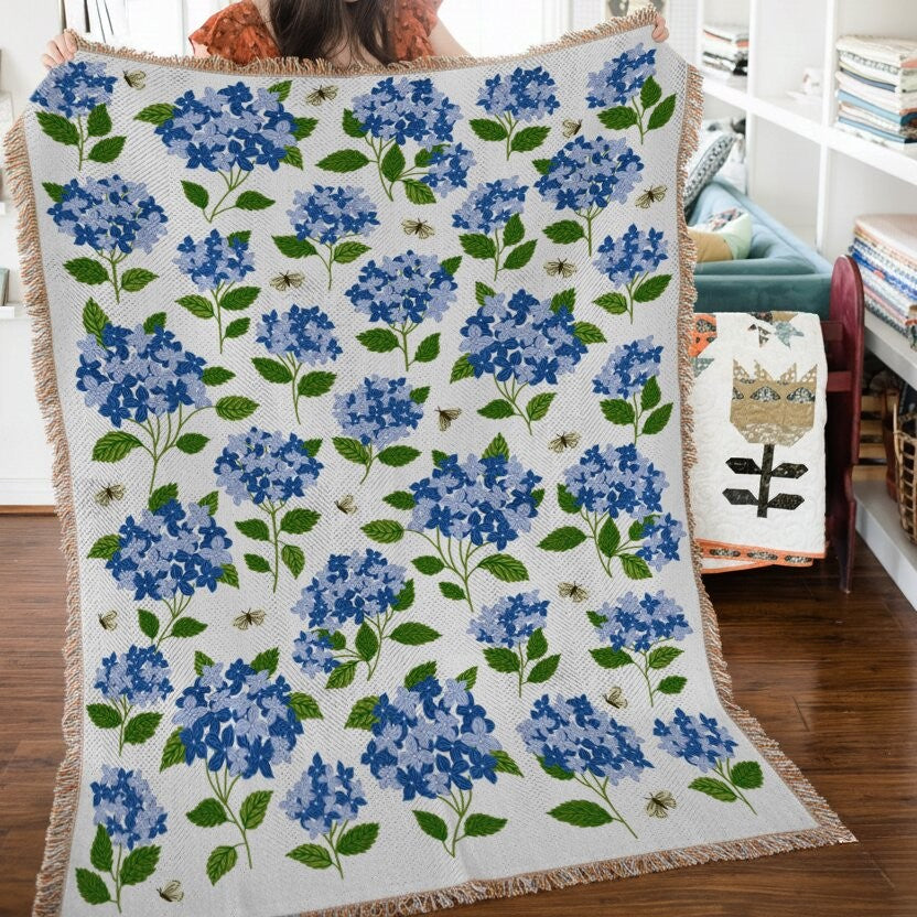 Floral-patterned throw blanket with blue flowers and green leaves on a wooden floor.