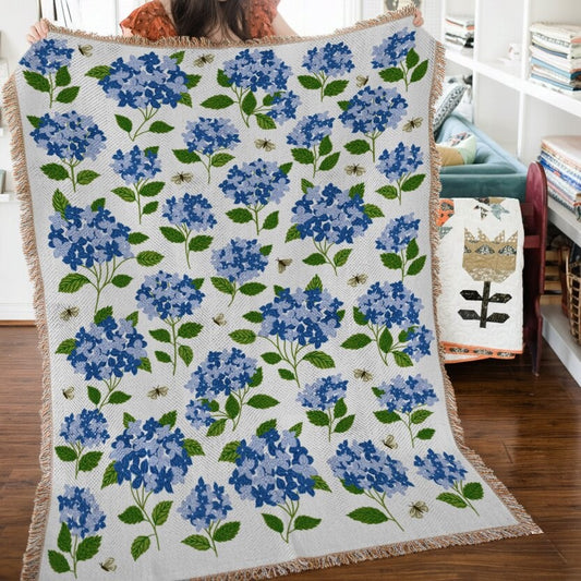 Floral-patterned throw blanket with blue flowers and green leaves on a wooden floor.