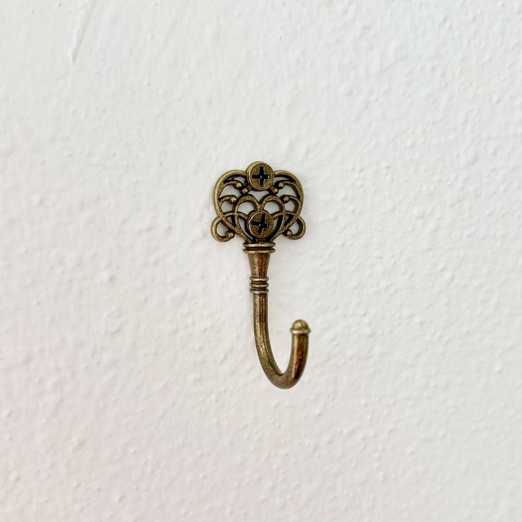 Decorative brass hook with intricate design on a white background