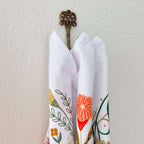 Three folded napkins with floral patterns hanging on a decorative hook against a white wall.