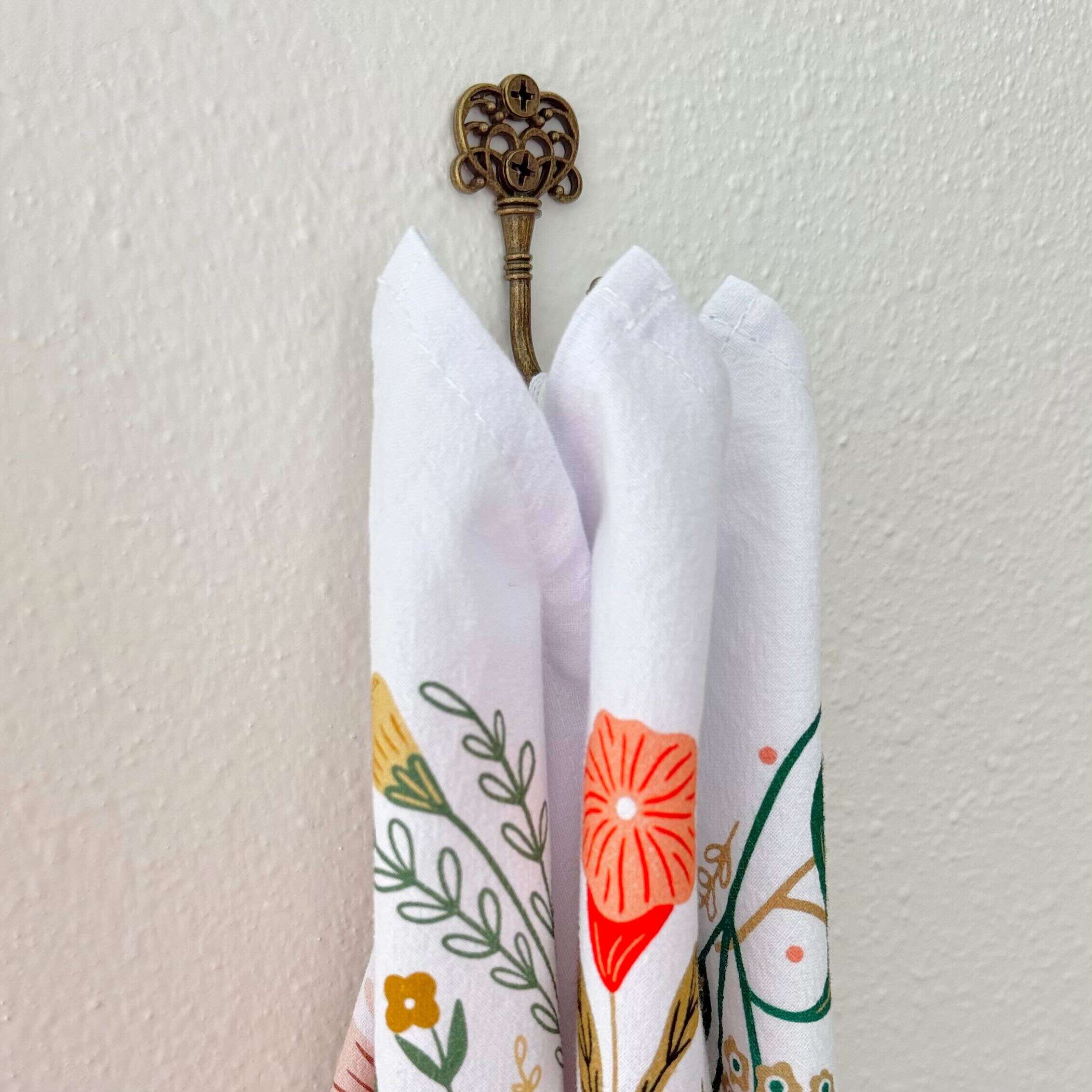 Three folded napkins with floral patterns hanging on a decorative hook against a white wall.