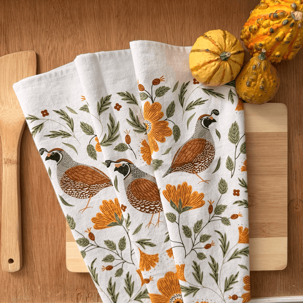 Set of three decorative towels with floral and bird patterns on a wooden surface with pumpkins.