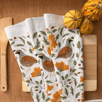 Set of three decorative towels with floral and bird patterns on a wooden surface with pumpkins.