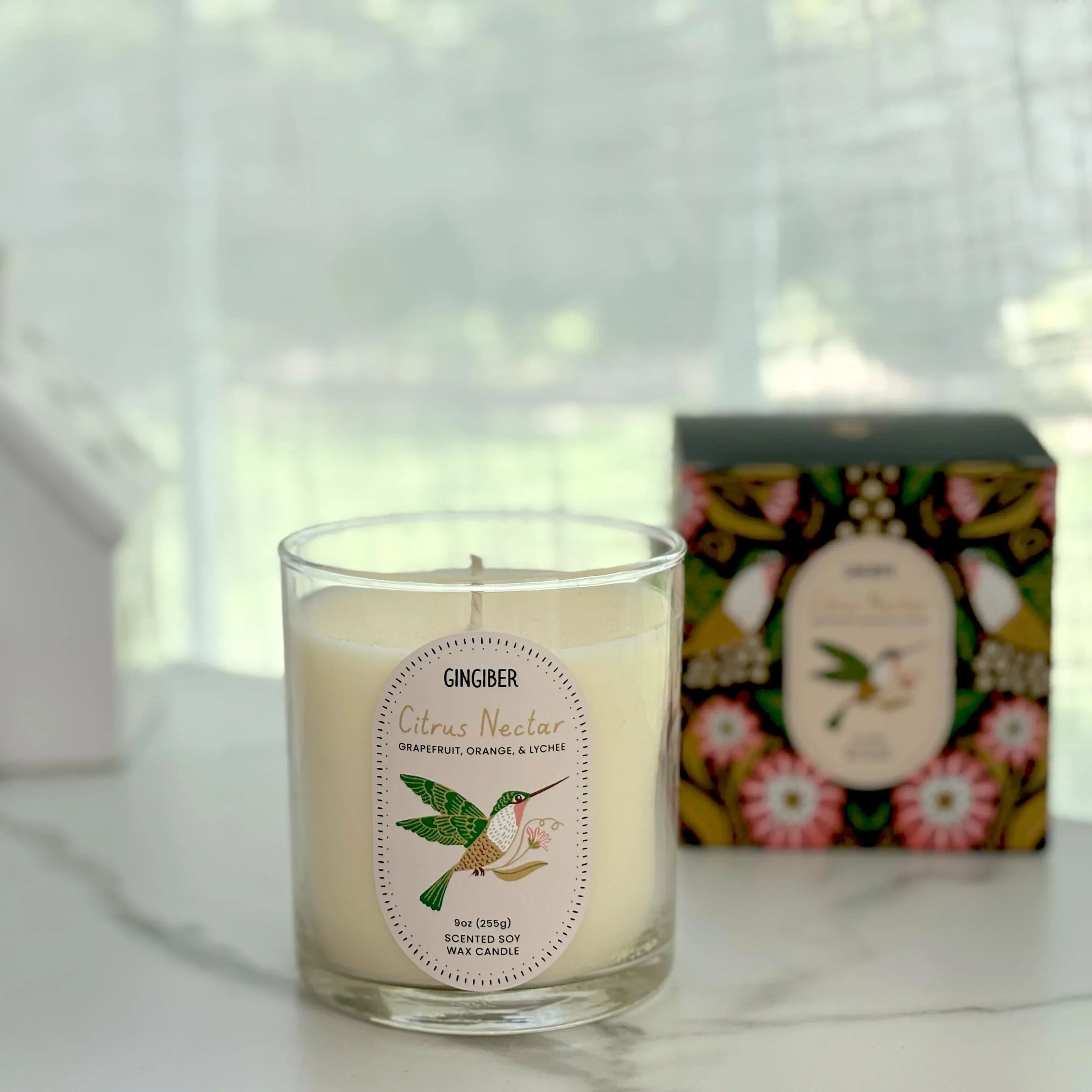 Glass cream-colored candle with green box and hummingbird illustration