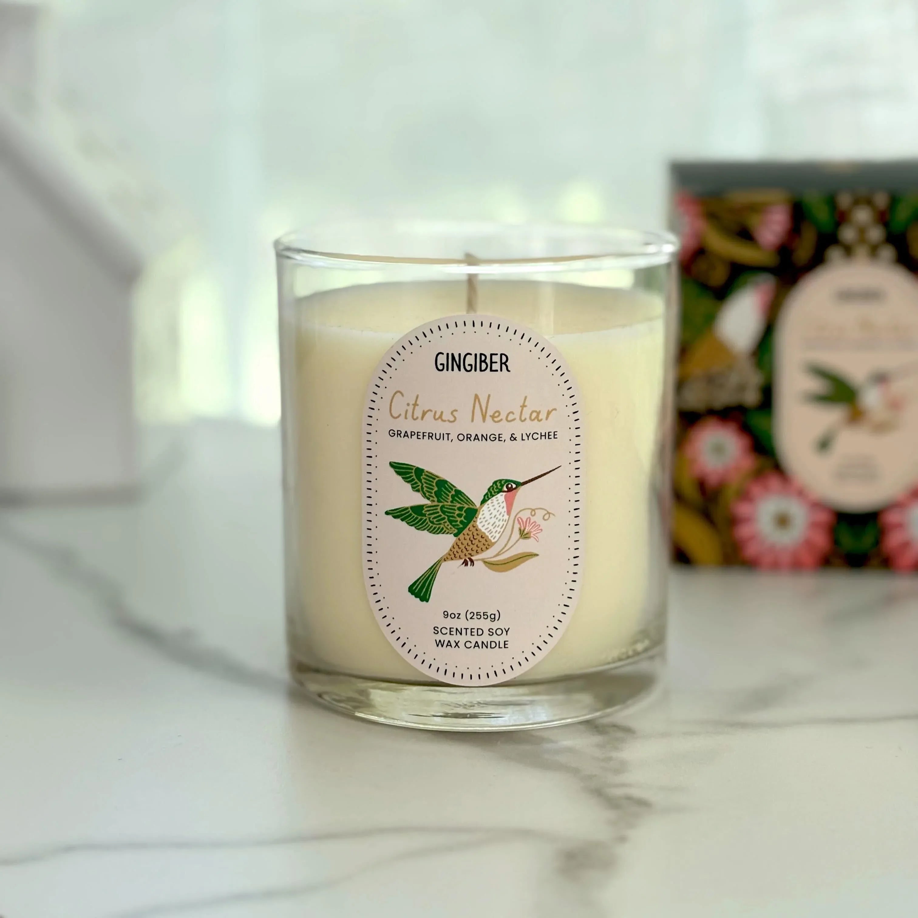 Glass cream-colored candle with green box and hummingbird illustration