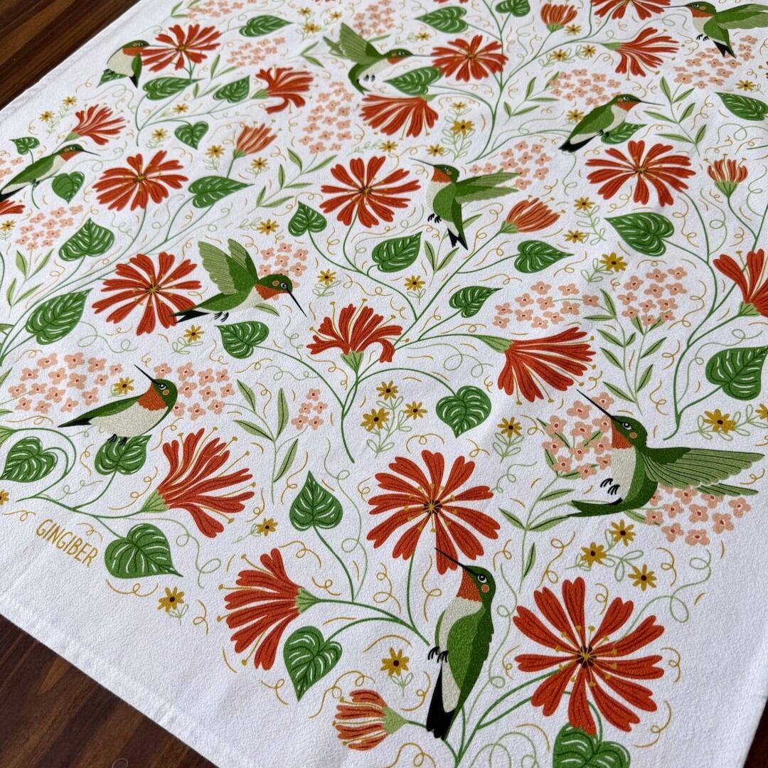 Decorative tablecloth with floral and hummingbird pattern on a wooden surface