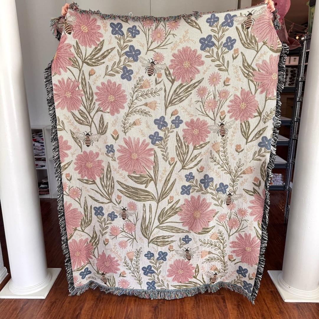 Floral patterned blanket with pink flowers and bees held up against a neutral background