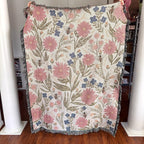 Floral patterned blanket with pink flowers and bees held up against a neutral background