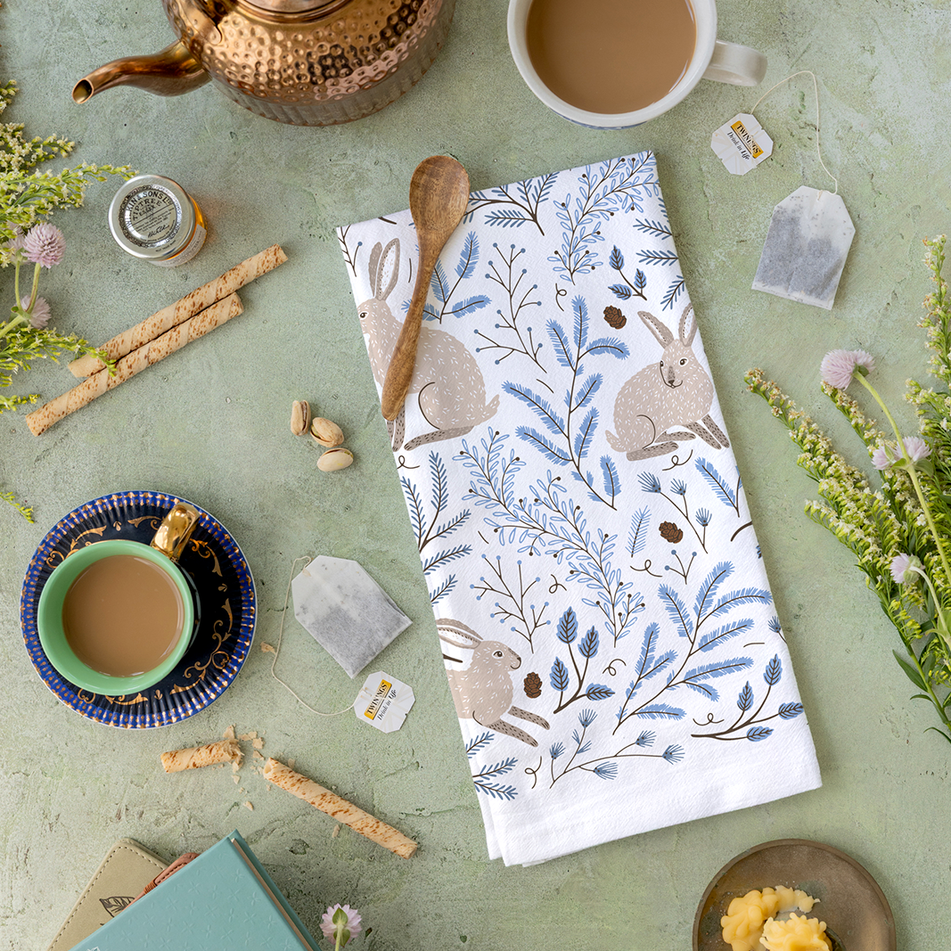 Tea towel with rabbit and floral pattern on a table with tea cups and snacks