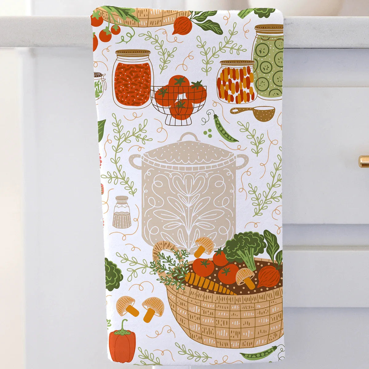 Kitchen towel with food-themed design featuring a pot, vegetables, and jars on a white background.