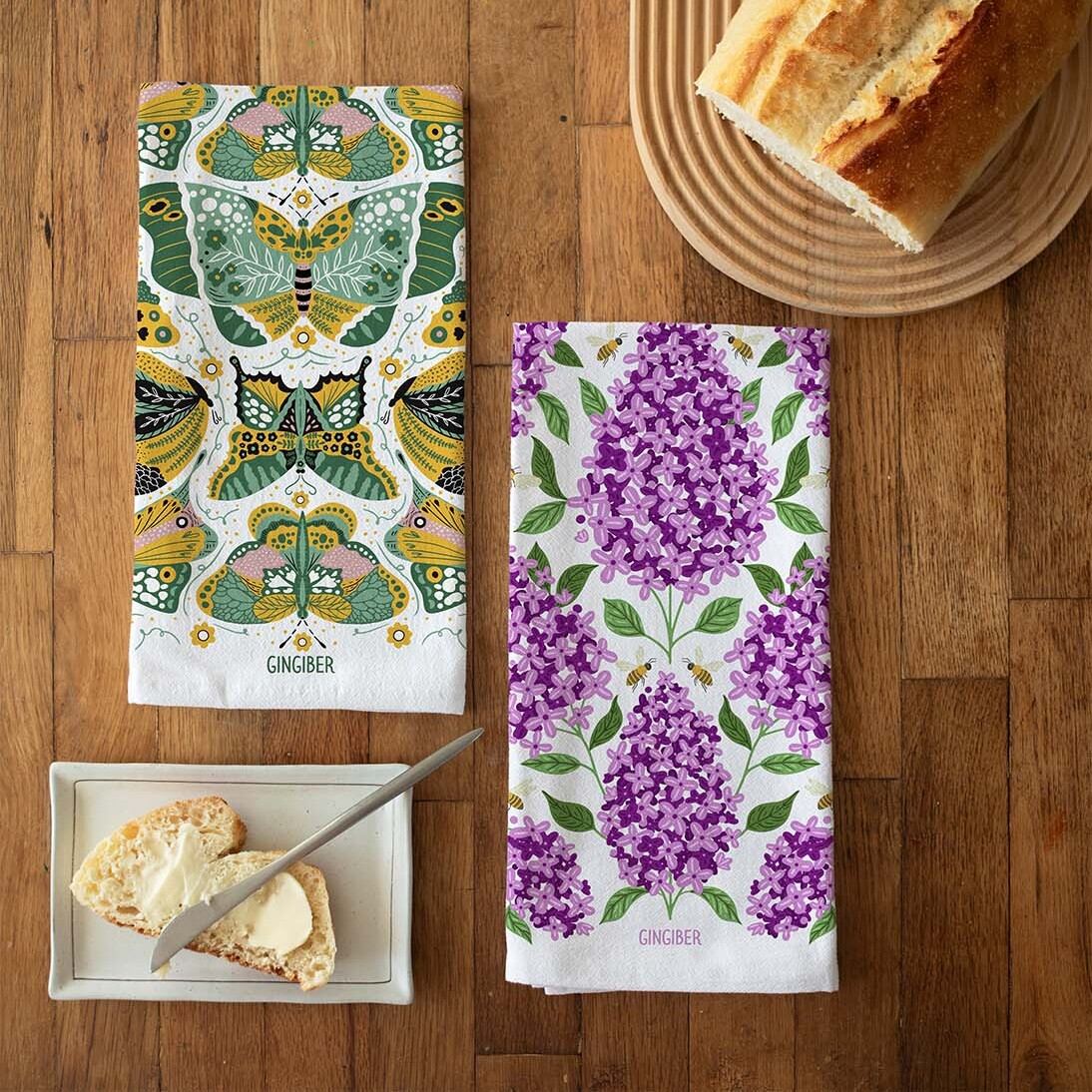 Two patterned towels on a wooden surface with bread and butter.