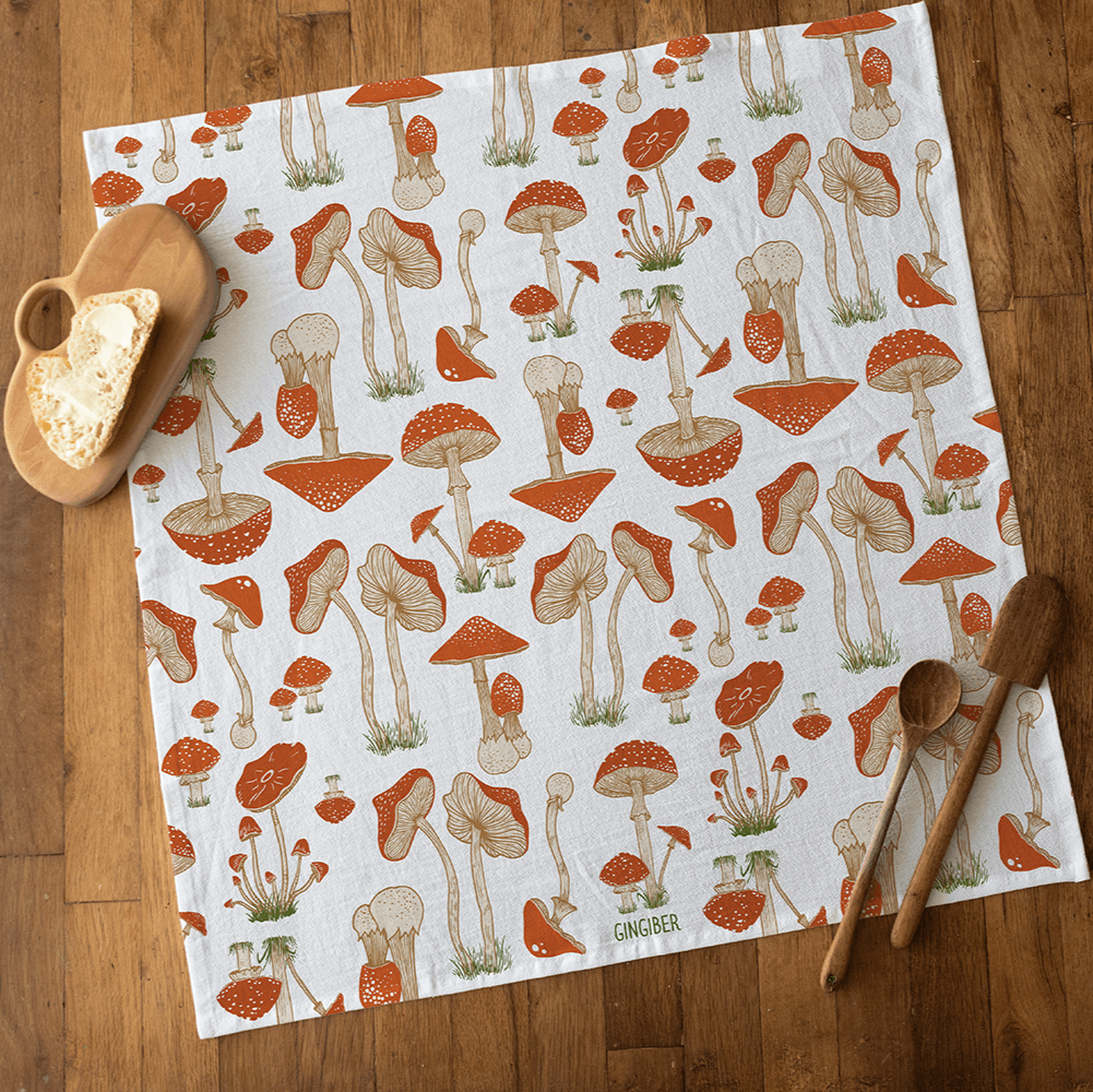 Mushroom-patterned towel on a wooden surface with wooden spoons and a candle.