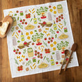 Decorative kitchen towel with food-themed illustrations on a wooden surface