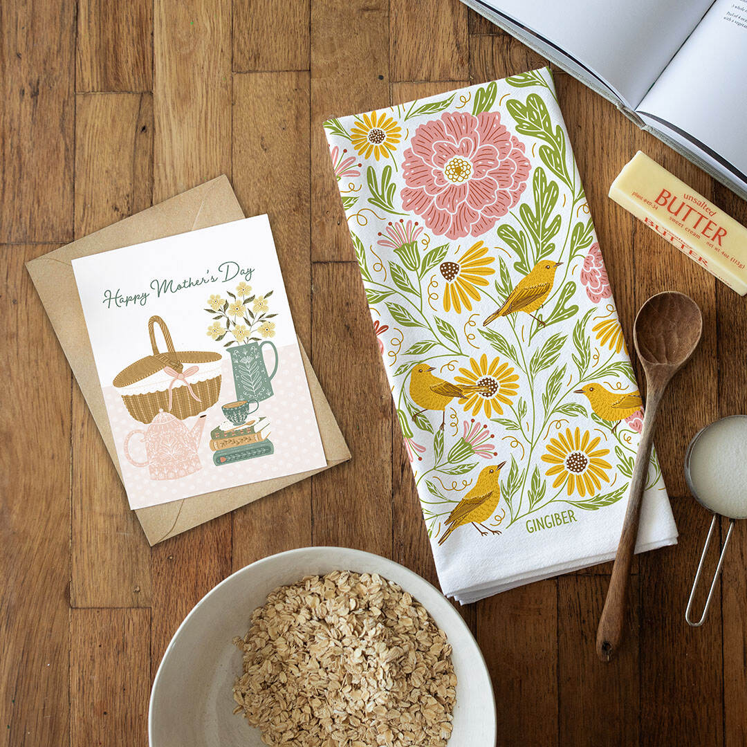 Floral towel with birds, card, bowl of oats, and wooden spoon on a wooden surface