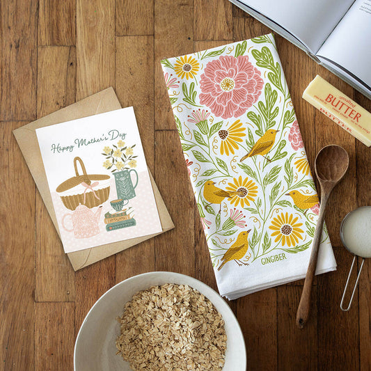 Floral towel with birds, card, bowl of oats, and wooden spoon on a wooden surface
