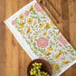 Decorative tea towel with floral and bird pattern on a wooden surface