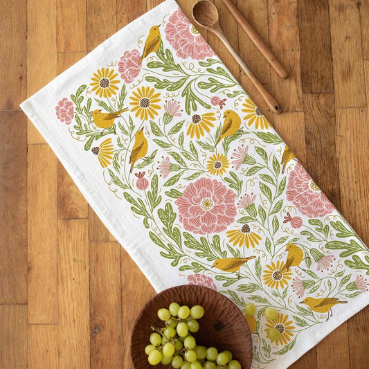 Decorative tea towel with floral and bird pattern on a wooden surface