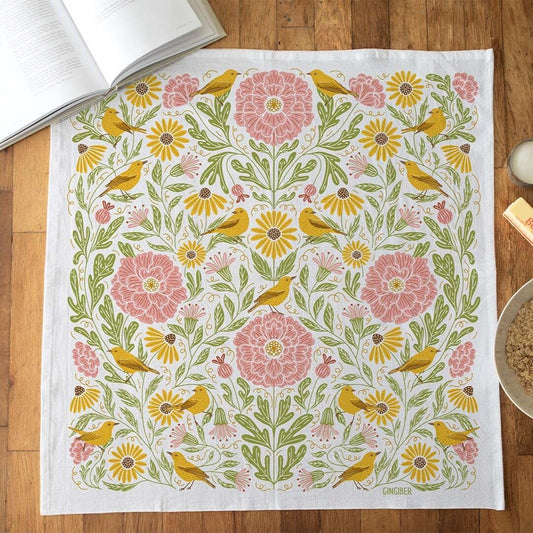 Floral and bird patterned towel on a wooden surface with books and a bowl.