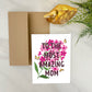 Greeting card with floral design and text 'To the most amazing mom' on a white background with a gold envelope and decorative elements.