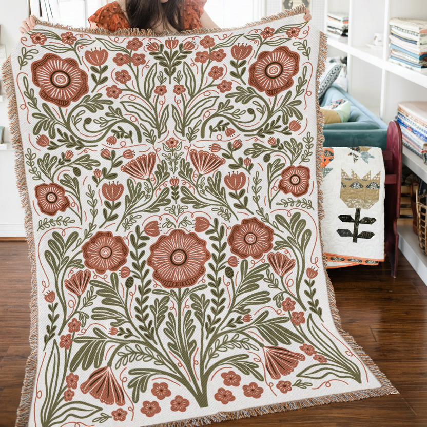 Woman holding a floral patterned blanket in a room with bookshelves and a couch.