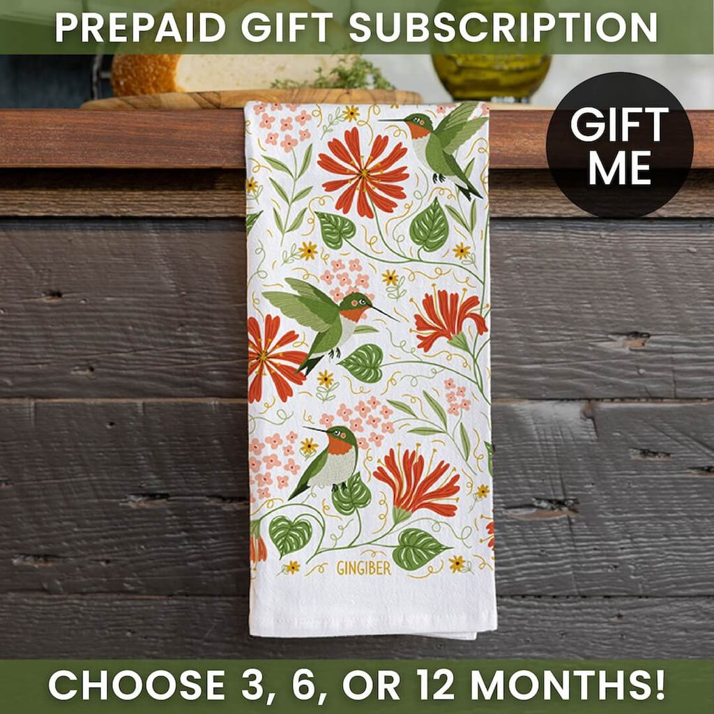 Floral towel with hummingbird design on a wooden surface, promotional text for prepaid gift subscription.