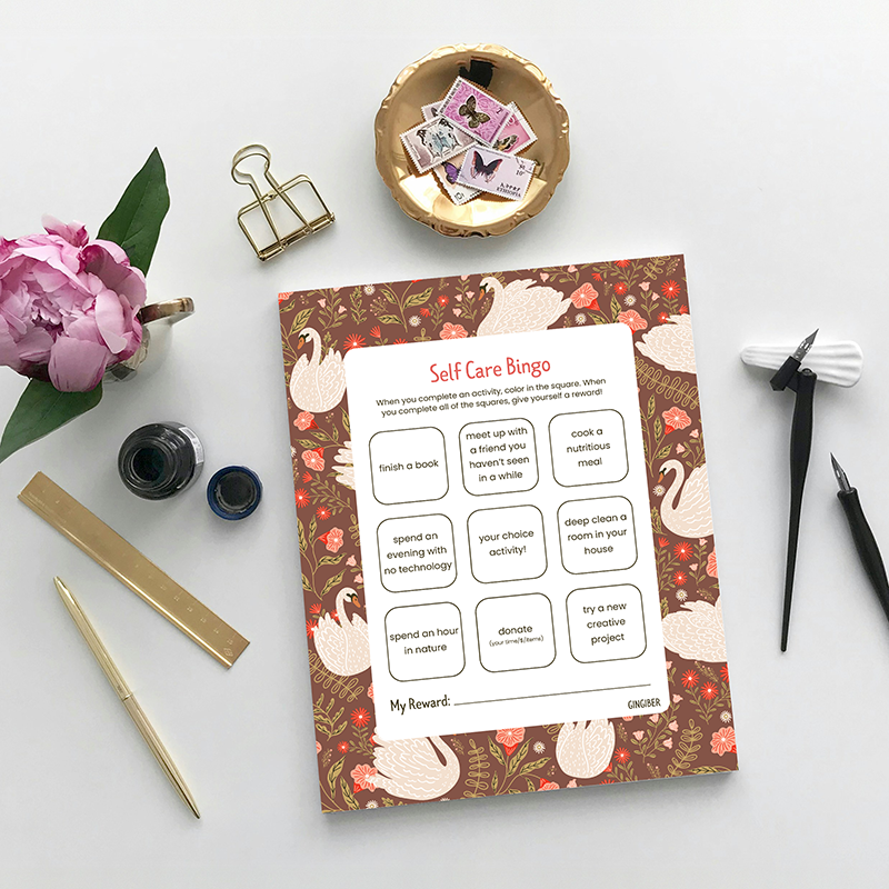 Self-care bingo sheet with swan design on a white surface with stationery items.