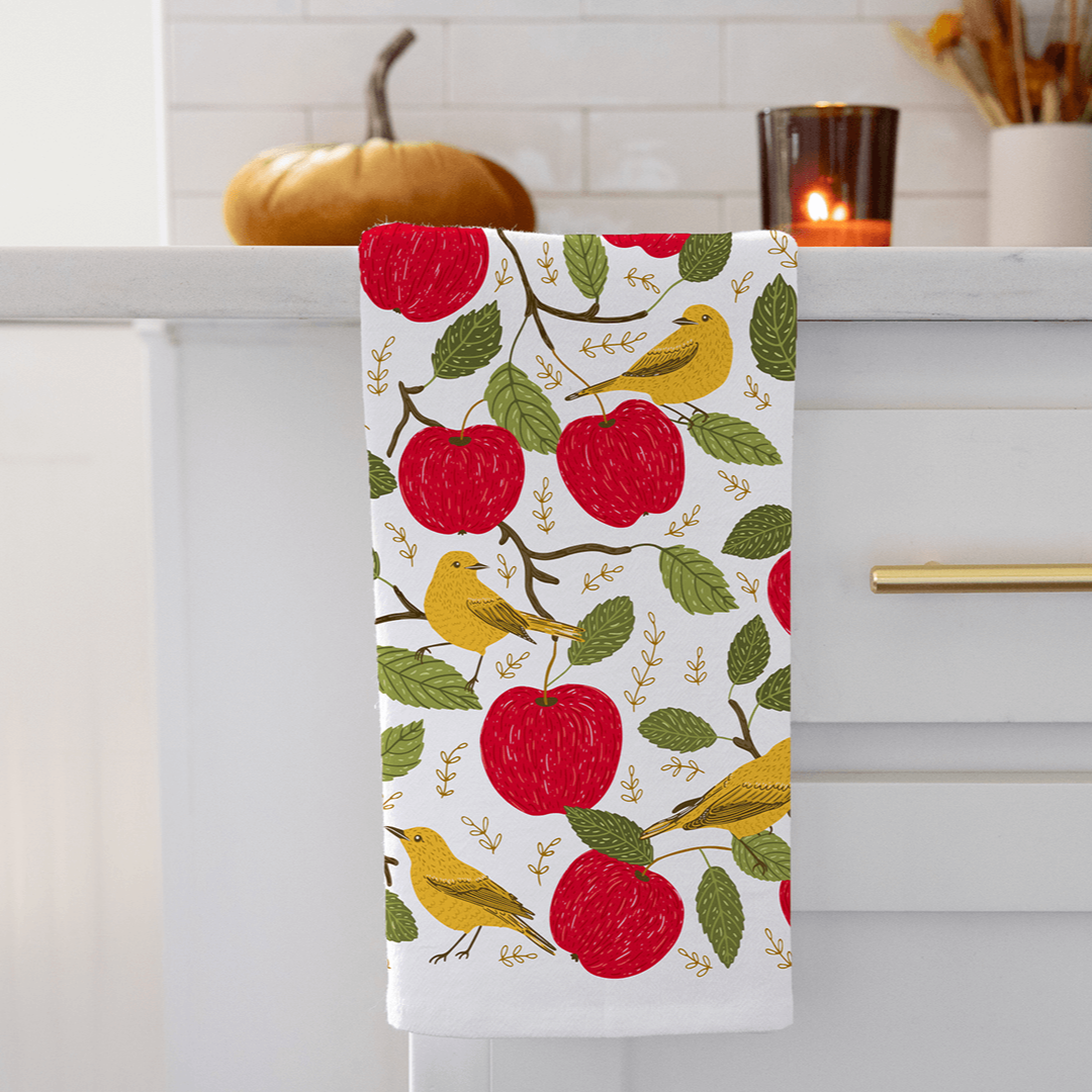 Decorative kitchen towel with apple and bird pattern hanging on a cabinet.