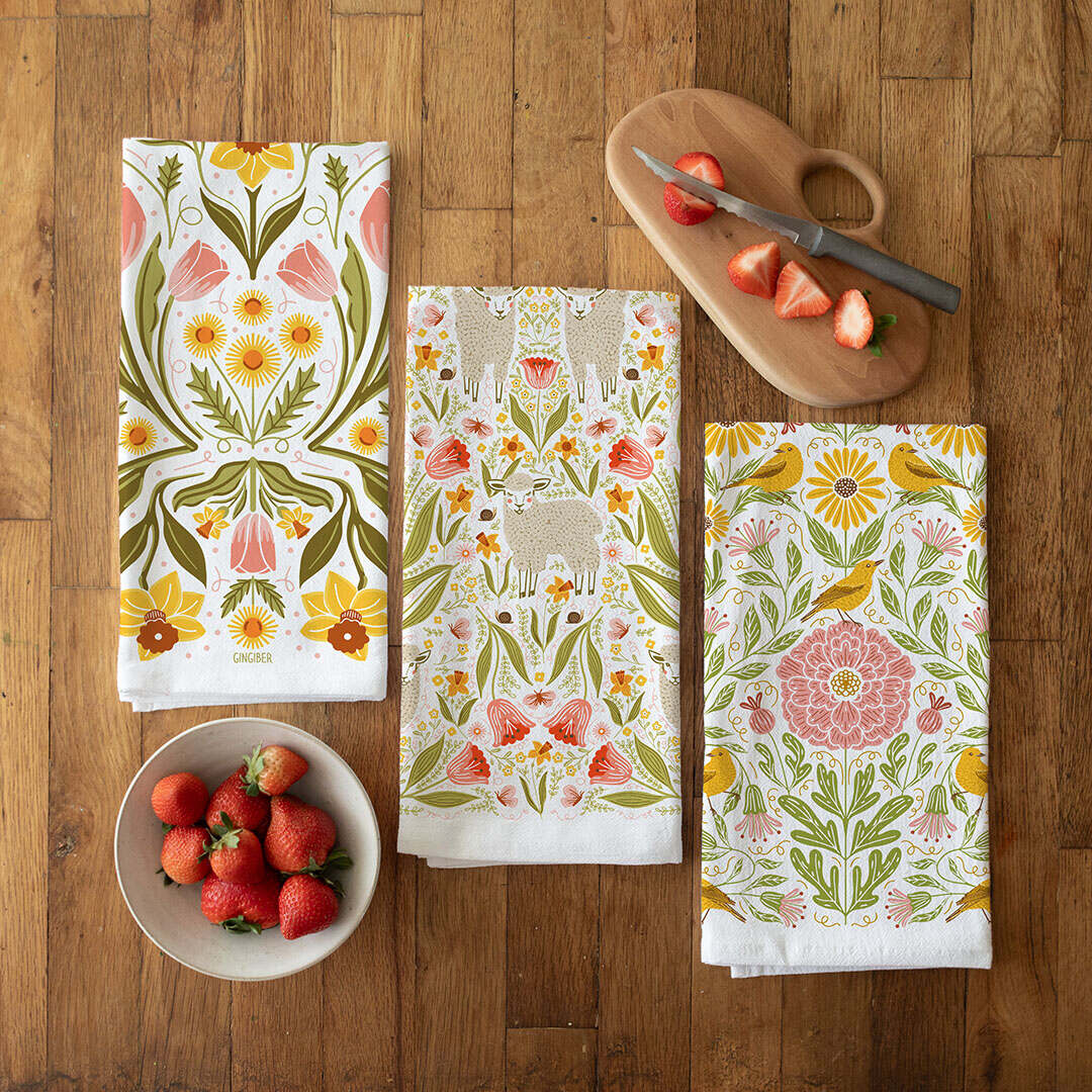 Set of floral patterned towels on a wooden table with strawberries and a cutting board.