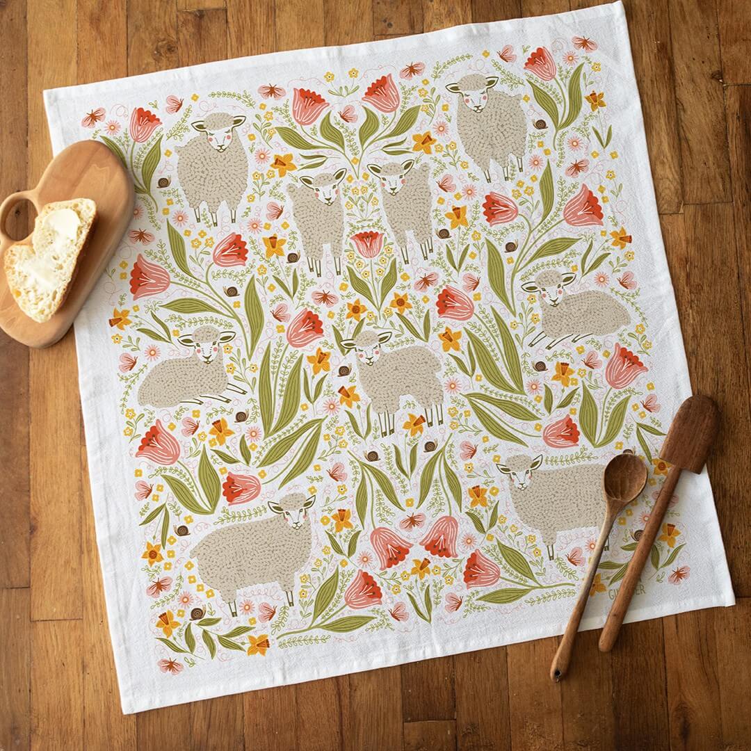 Decorative towel with sheep and floral pattern on a wooden surface