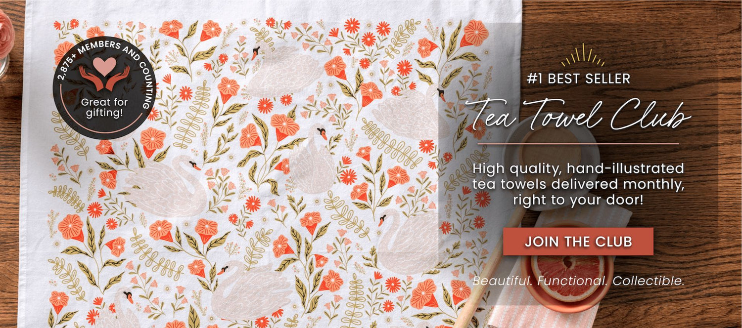 Tea towel with floral pattern and promotional text for Tea Towel Club on a wooden surface