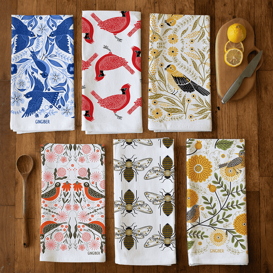 Set of six patterned towels on a wooden surface with a cutting board and lemon.