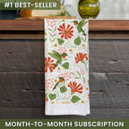 Floral towel with hummingbird design on a wooden surface, featuring the brand 'Gingiber'.