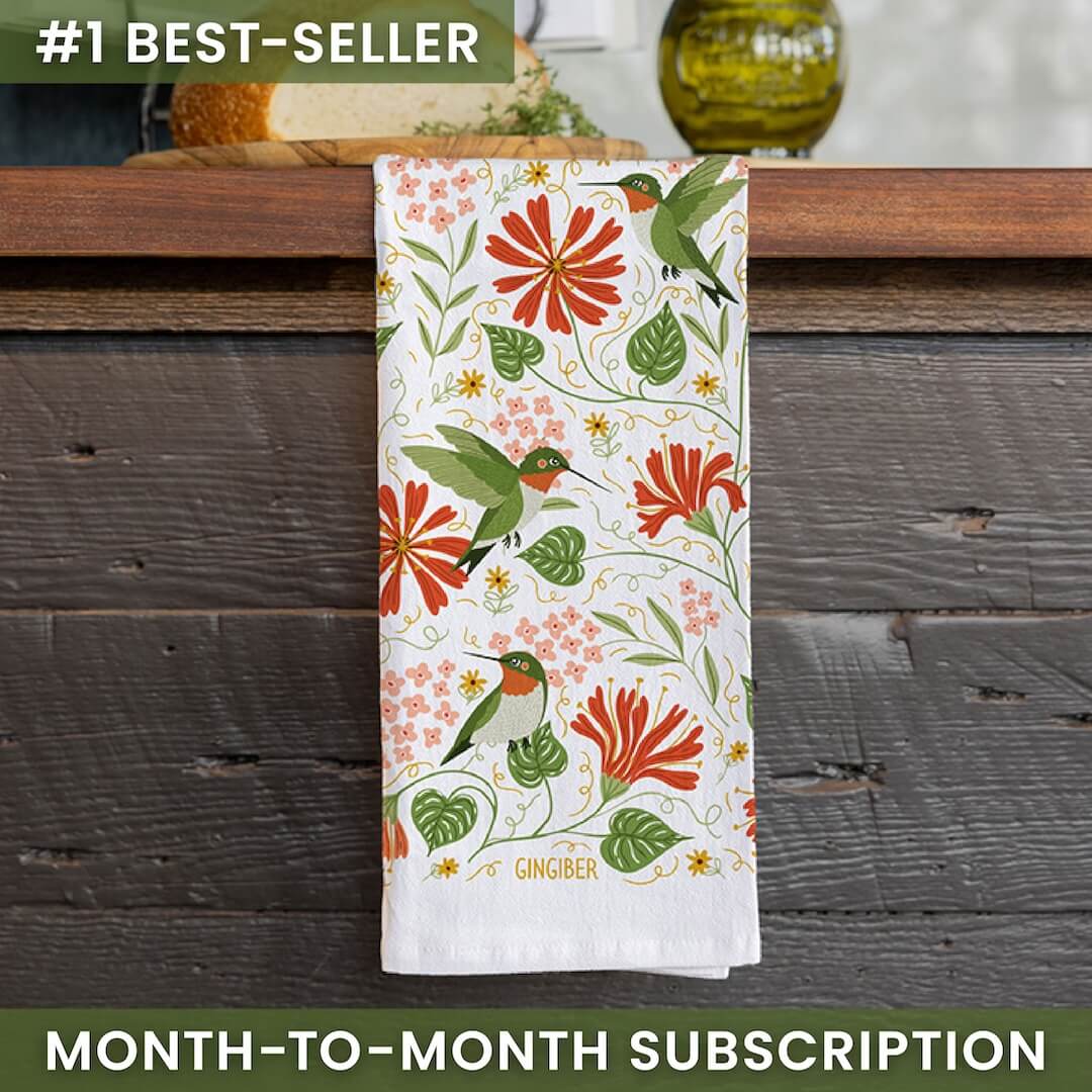 Floral towel with hummingbird design on a wooden surface, featuring the brand 'Gingiber'.