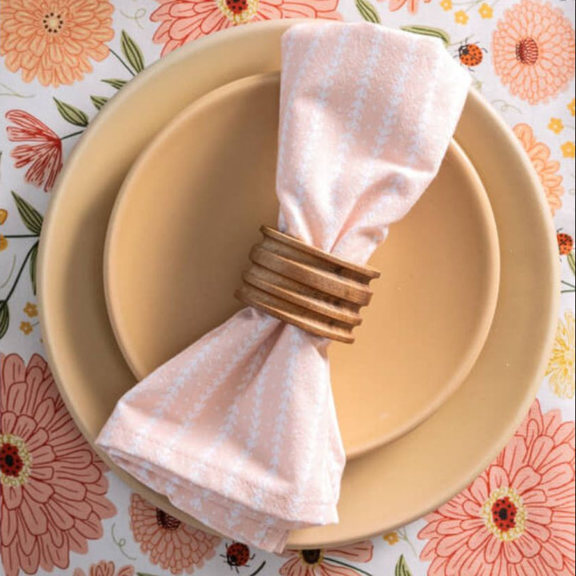 Napkin folded on a gold napkin ring with a floral patterned tablecloth in the background