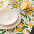 Dining table setting with lemon-themed placemat, white plates, and a bowl of lemons.