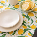 Dining table setting with lemon-themed placemat, white plates, and a bowl of lemons.